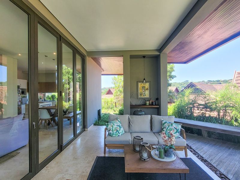 A spacious covered patio featuring stone flooring, a timber ceiling, and large glass sliding doors that provide seamless indoor-outdoor flow.