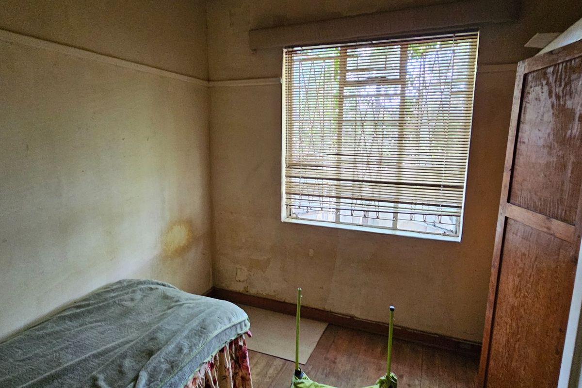 A bedroom featuring wooden flooring, a window with fitted blinds, and a built-in wooden door, requiring cosmetic updates and wall repairs.