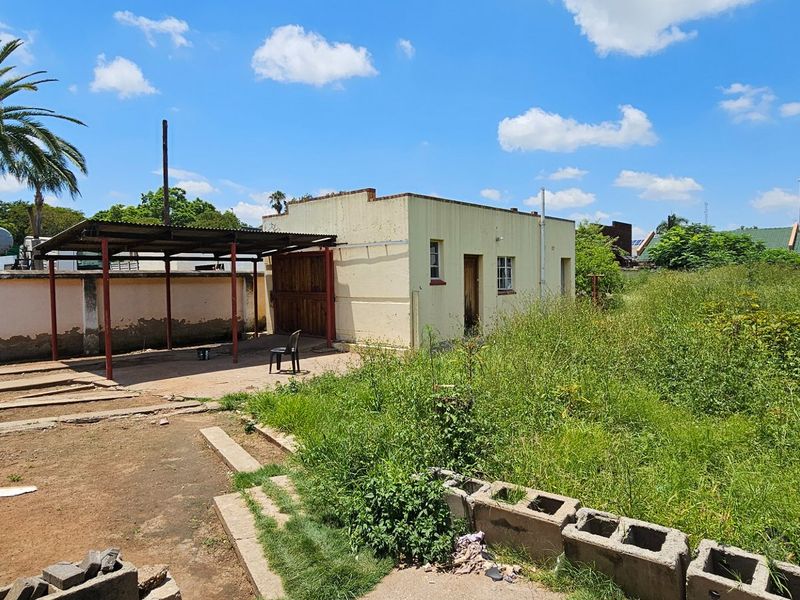 Rear view of the property featuring a detached outbuilding, a covered carport area, and an expansive, unmaintained garden space.