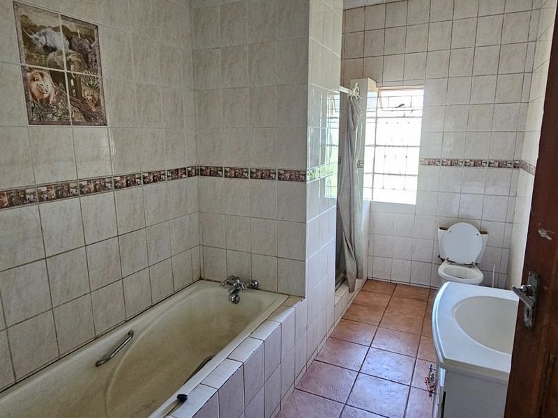 A dated bathroom featuring a built-in bathtub, tiled walls with decorative accents, a toilet, and a vanity basin.