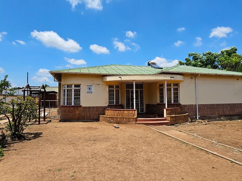 Front view of a single-story house featuring a covered porch, brick facade detailing, and a metal roof with a solar water heater.