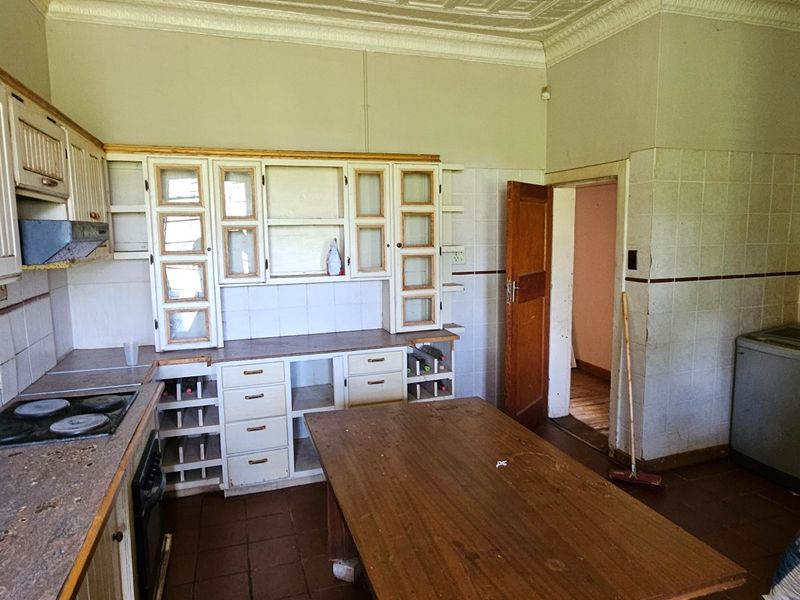A dated kitchen featuring traditional cabinetry, tiled splashbacks, and a built-in hob, offering significant potential for renovation and modernization.