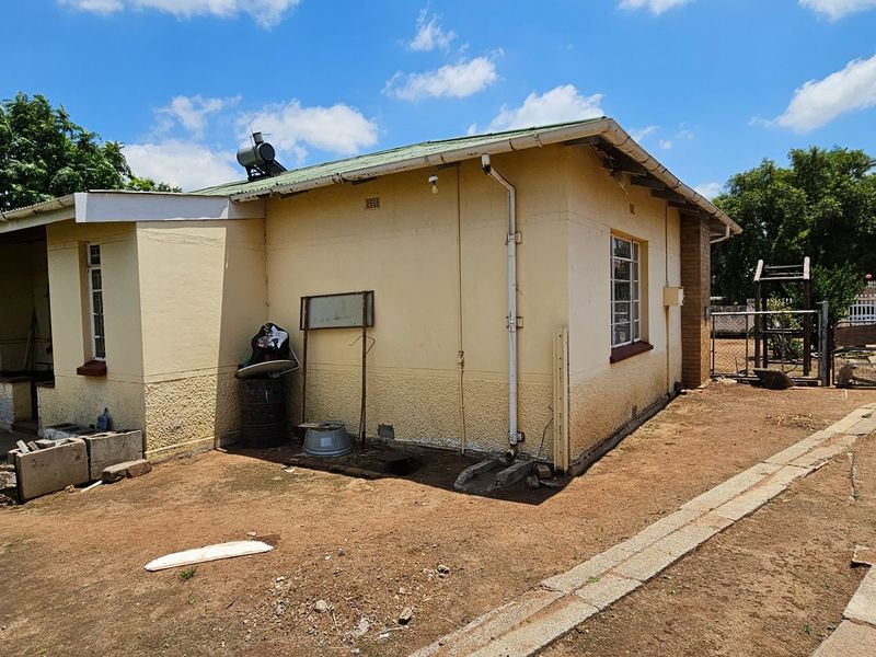 Rear exterior view of the house featuring a covered patio area, solar water heater, and surrounding yard space with concrete pathways.