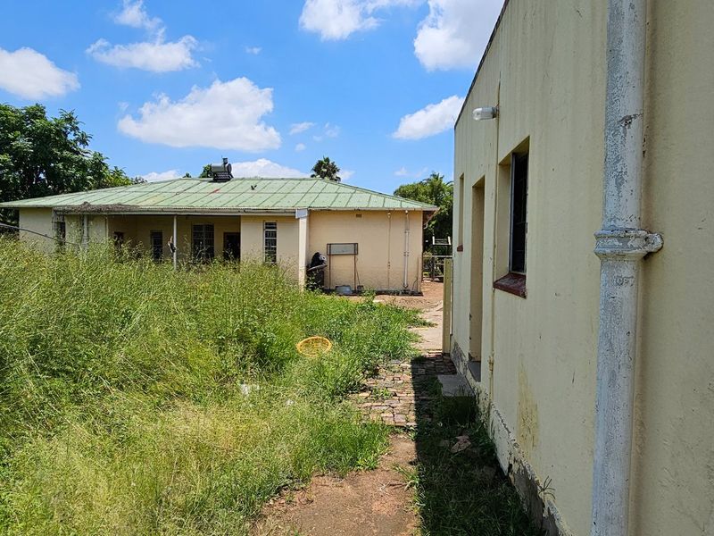 Rear view of the property showing the main house structure, a secondary building, and an overgrown garden area requiring significant landscaping and maintenance.