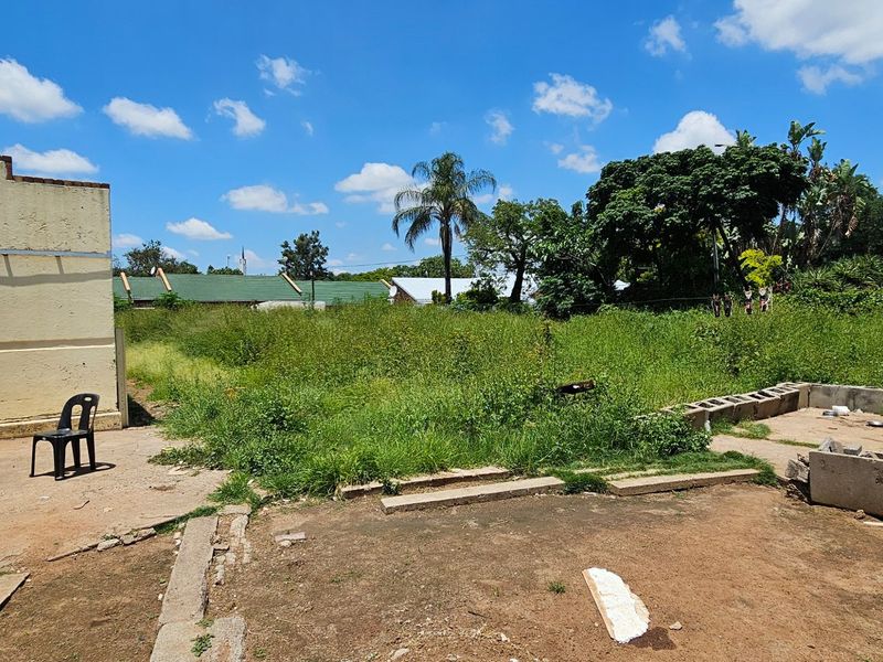 Rear exterior view of the property featuring a large, overgrown garden area, concrete patio space, and weathered exterior building walls.