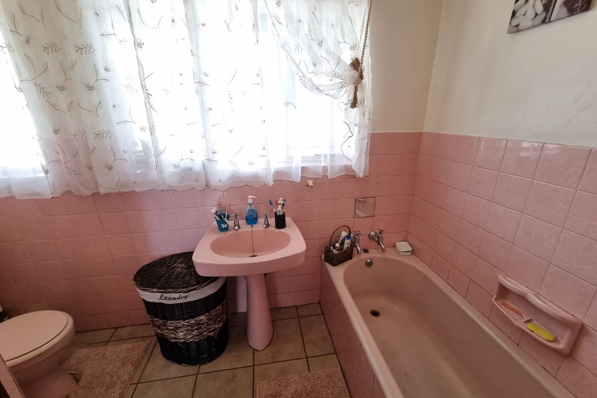 A dated bathroom featuring a vintage pink pedestal sink, matching bathtub, and pink wall tiles with tiled-in soap dish.