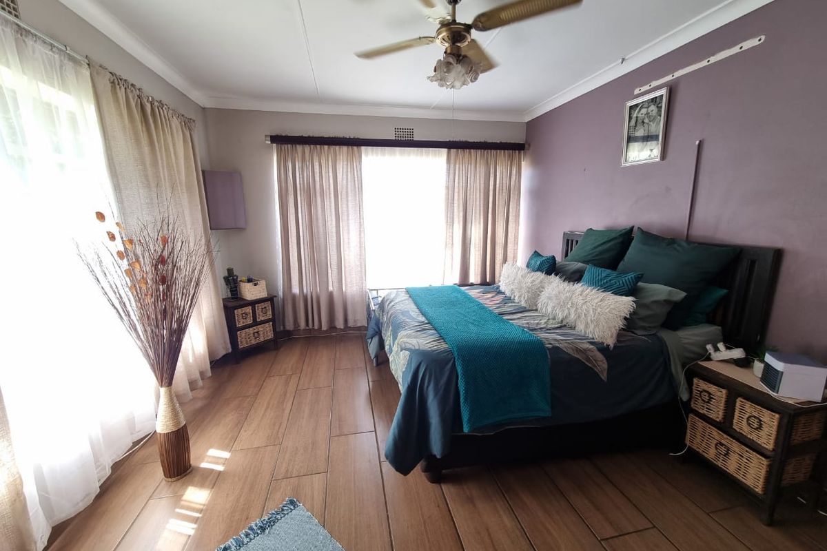 Spacious bedroom featuring wood-look tiled flooring, a ceiling fan, and large windows allowing for ample natural light.