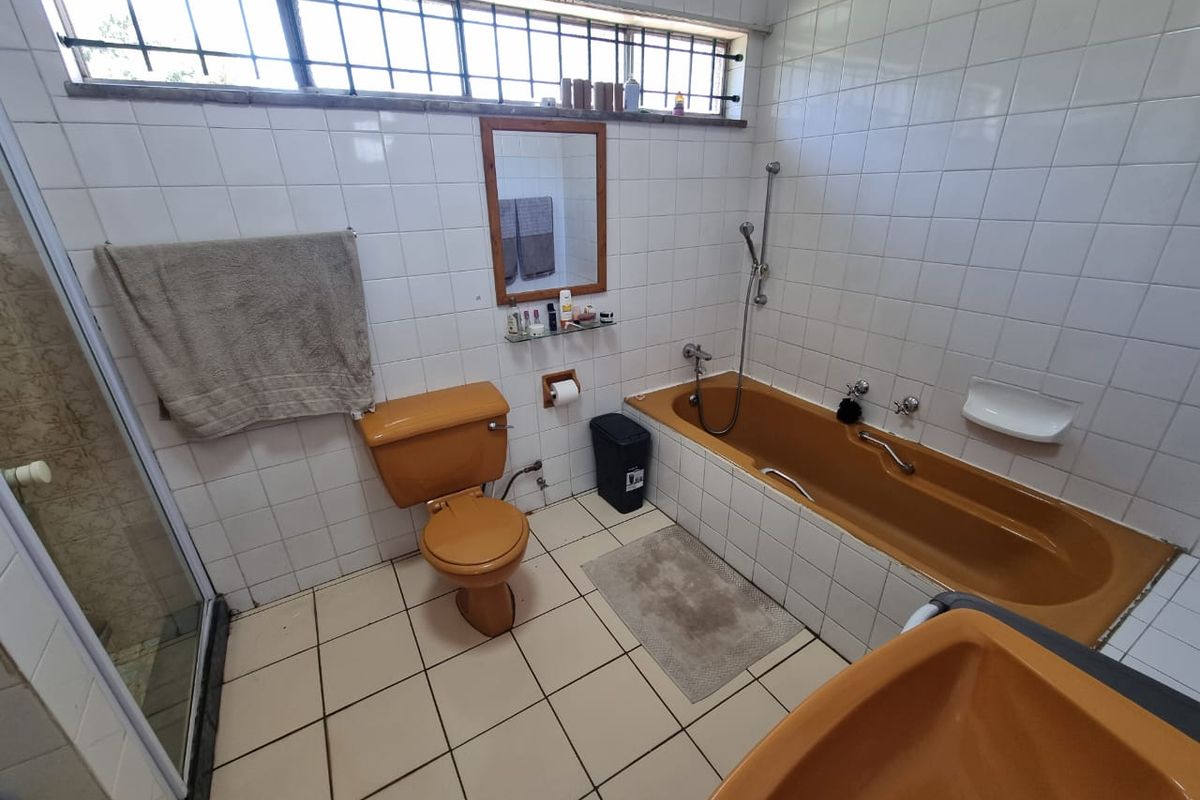 A dated bathroom featuring original mustard-colored sanitary ware, including a bathtub, toilet, and basin, complemented by white wall tiles and a security-grilled window.