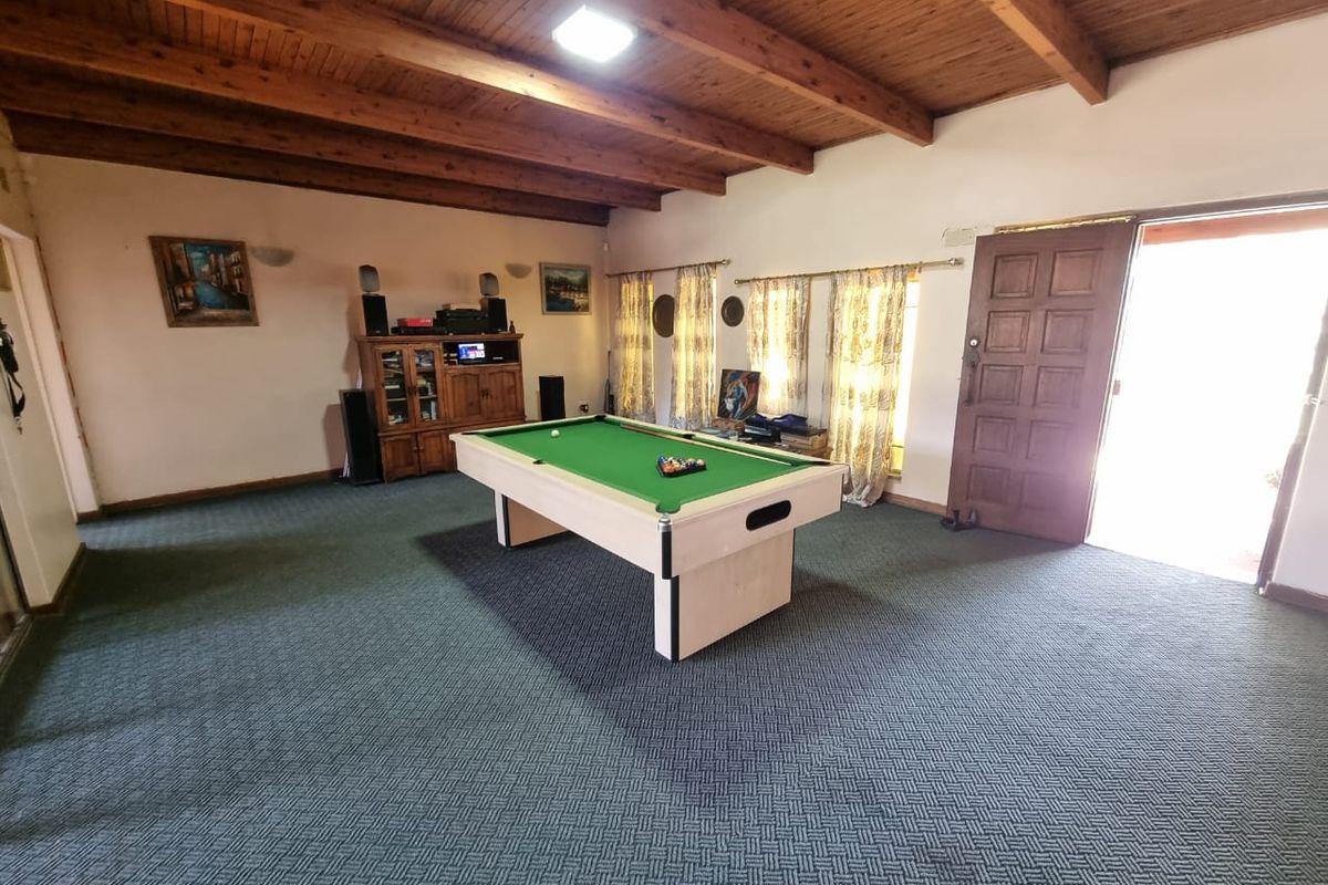 Spacious living area featuring exposed timber beam ceilings and wall-to-wall carpeting, with direct access to the exterior through a solid timber door.