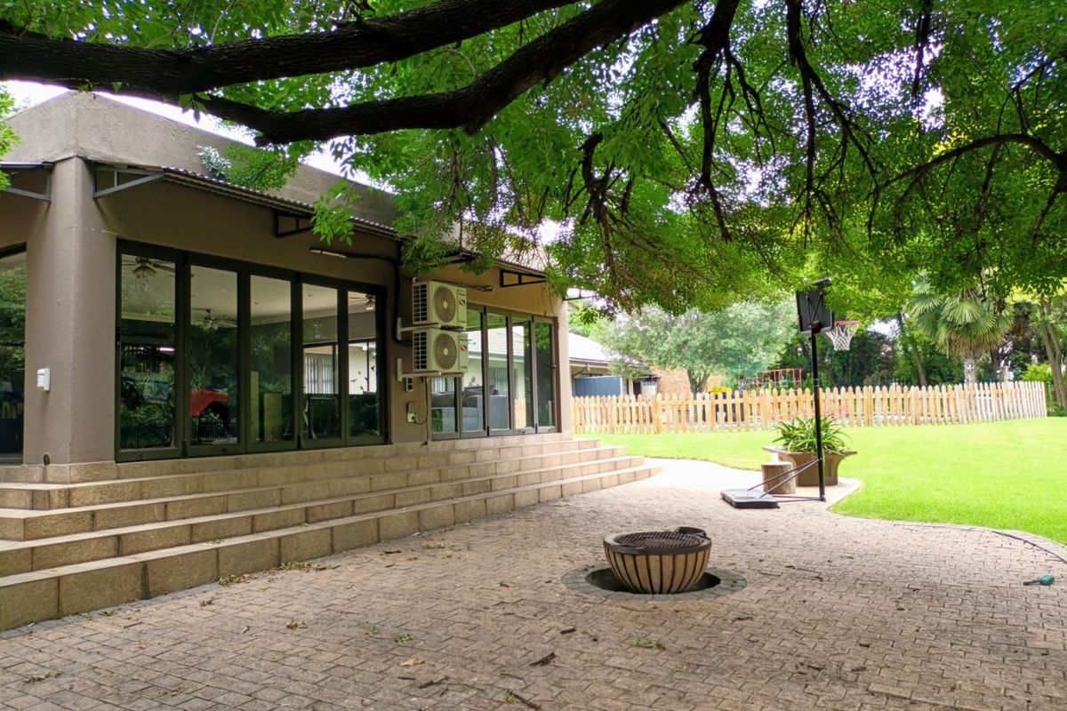 Spacious rear patio featuring paved flooring, built-in fire pit, and large glass sliding doors leading into the home, set within a landscaped garden.