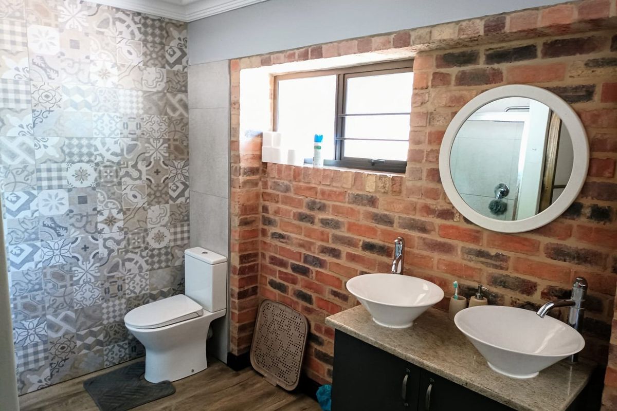 A modern bathroom featuring a double vanity with vessel sinks, exposed brick wall detailing, and decorative patterned wall tiles.