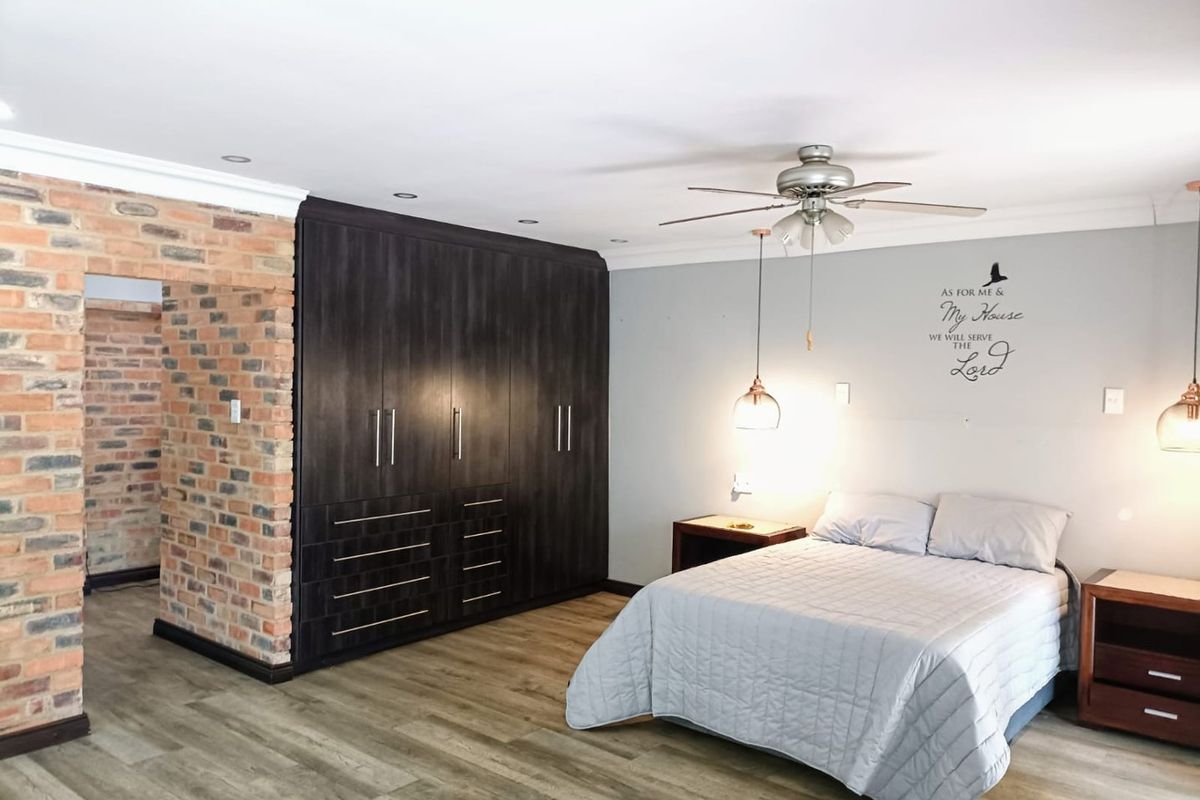 Spacious bedroom featuring built-in dark wood cabinetry, exposed brick feature wall, recessed ceiling lighting, and a ceiling fan.