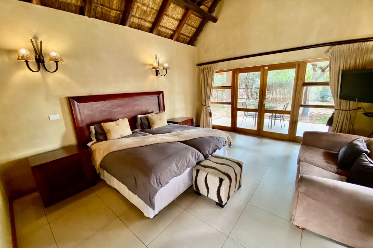 Spacious bedroom featuring a high vaulted thatched ceiling, tiled flooring, and large glass sliding doors providing direct access to the outdoor patio area.