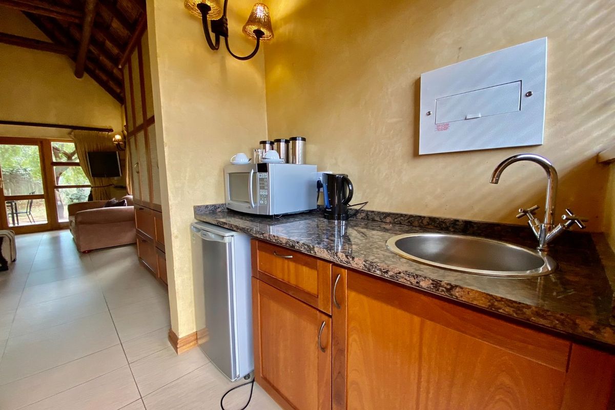 A compact kitchenette area featuring wooden cabinetry, granite countertops, a stainless steel sink, and a vaulted ceiling with exposed timber beams.