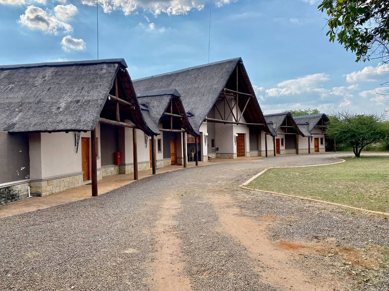 Exterior view of a lodge-style building featuring a distinctive thatched roof, timber support beams, and stone base detailing along the facade.