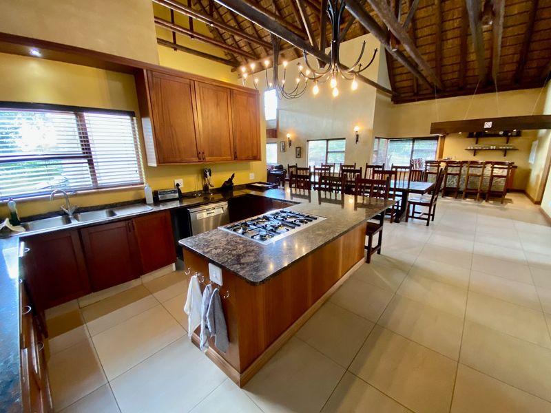 Spacious open-plan kitchen and dining area featuring a central island with a built-in gas hob, wooden cabinetry, and a high vaulted thatched ceiling.