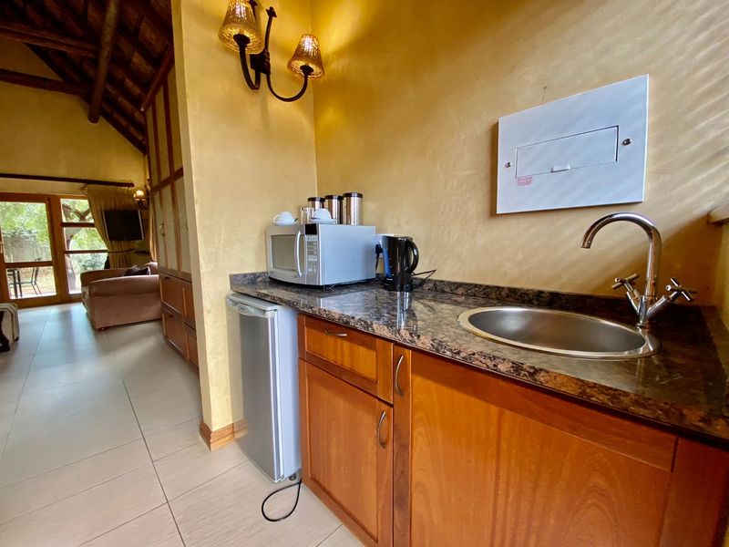 A compact kitchenette area featuring wooden cabinetry, granite countertops, a stainless steel sink, and a vaulted ceiling with exposed timber beams.