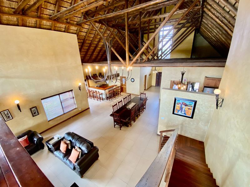 Spacious open-plan living and dining area featuring a high vaulted thatched roof with exposed timber trusses and tiled flooring.