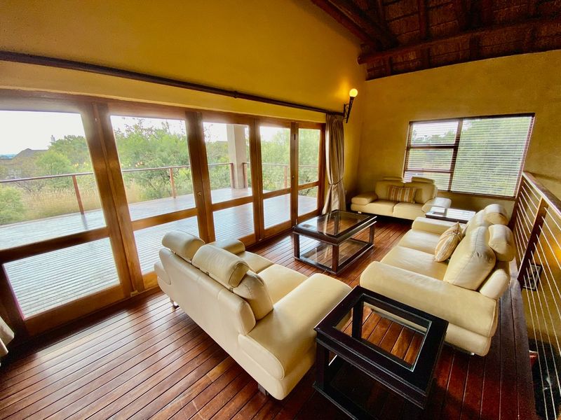 Spacious living area featuring warm timber flooring, high vaulted thatched ceiling, and large glass sliding doors opening onto an expansive wooden deck.