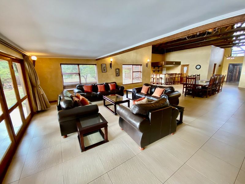 Spacious open-plan living and dining area featuring tiled flooring, exposed timber ceiling beams, and a built-in bar area.