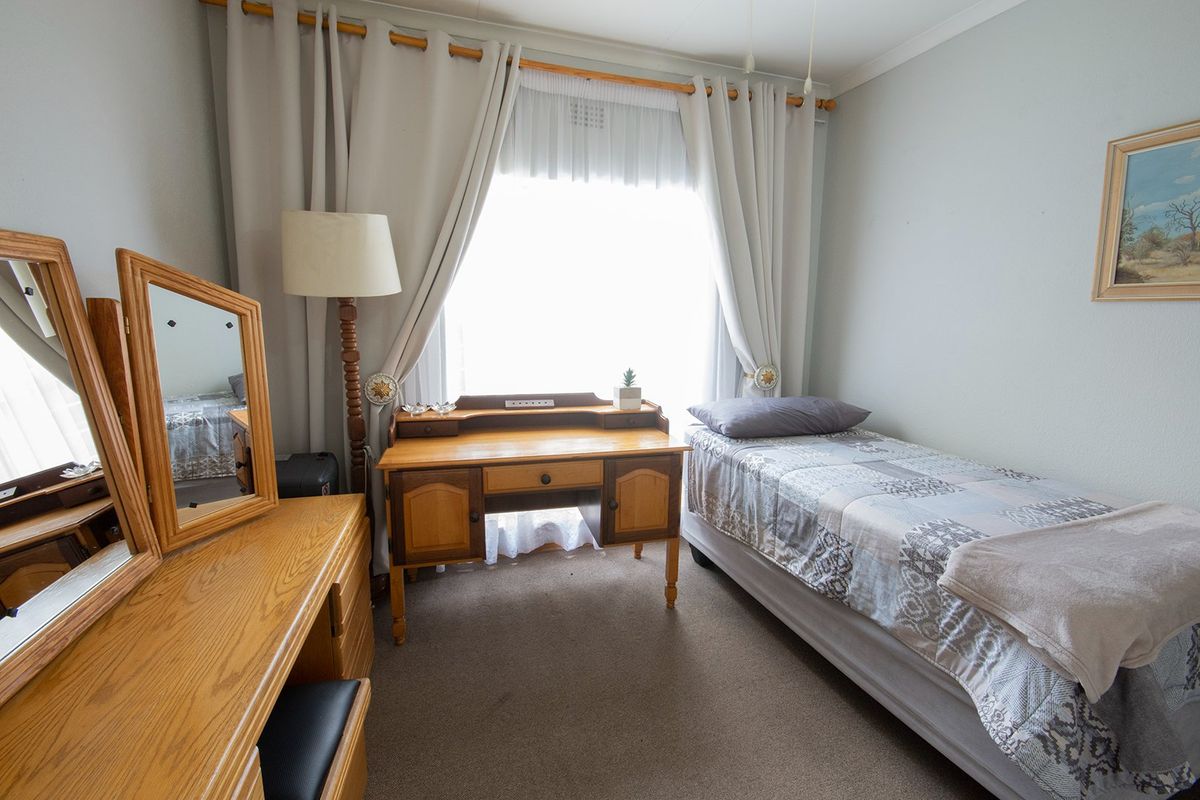 A functional bedroom featuring neutral wall finishes, carpeted flooring, and a large window with curtain treatments.