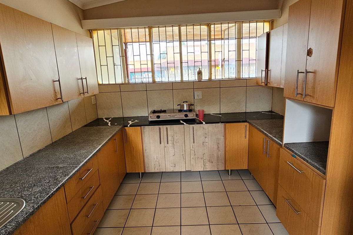 A functional kitchen featuring wood-finish cabinetry, granite countertops, tiled flooring, and a built-in hob, offering a practical layout for daily meal preparation.