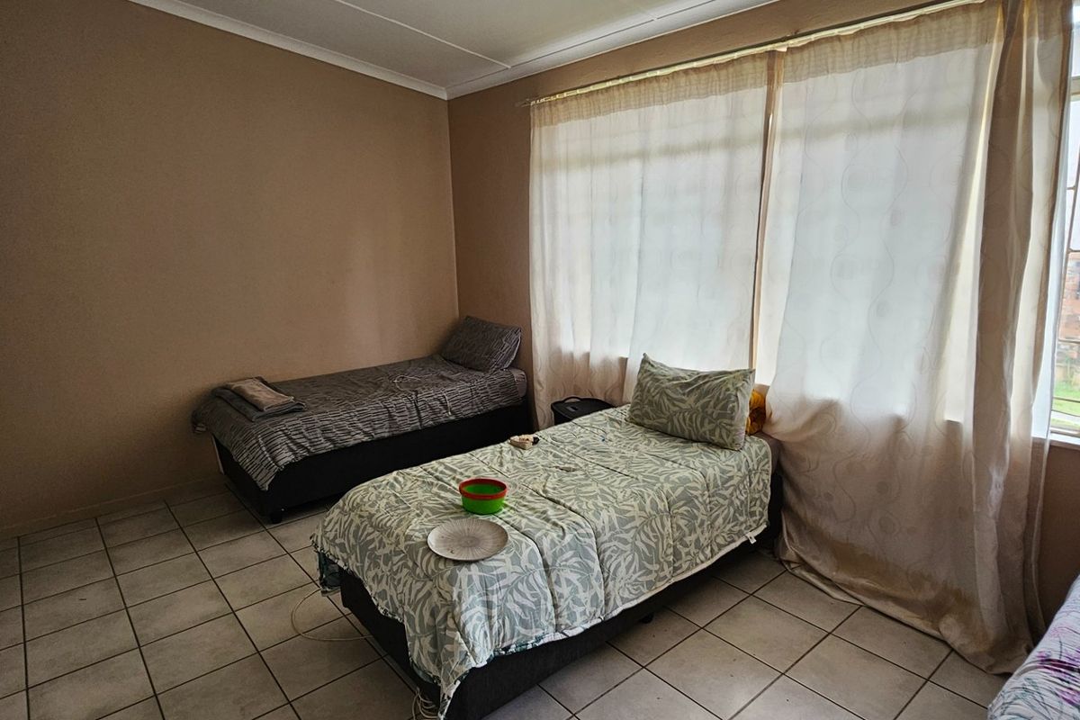 A functional bedroom featuring tiled flooring, built-in wardrobe storage, and large windows with curtains allowing for natural light.