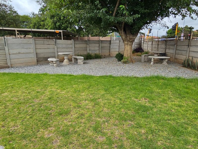 A private rear garden featuring a lawn area, gravel landscaping, mature tree, and secure perimeter precast concrete walling with electric fencing.