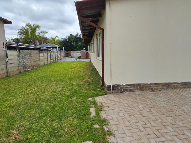 A side view of the property featuring a paved walkway, a grass lawn, and a perimeter boundary wall with electric fencing.