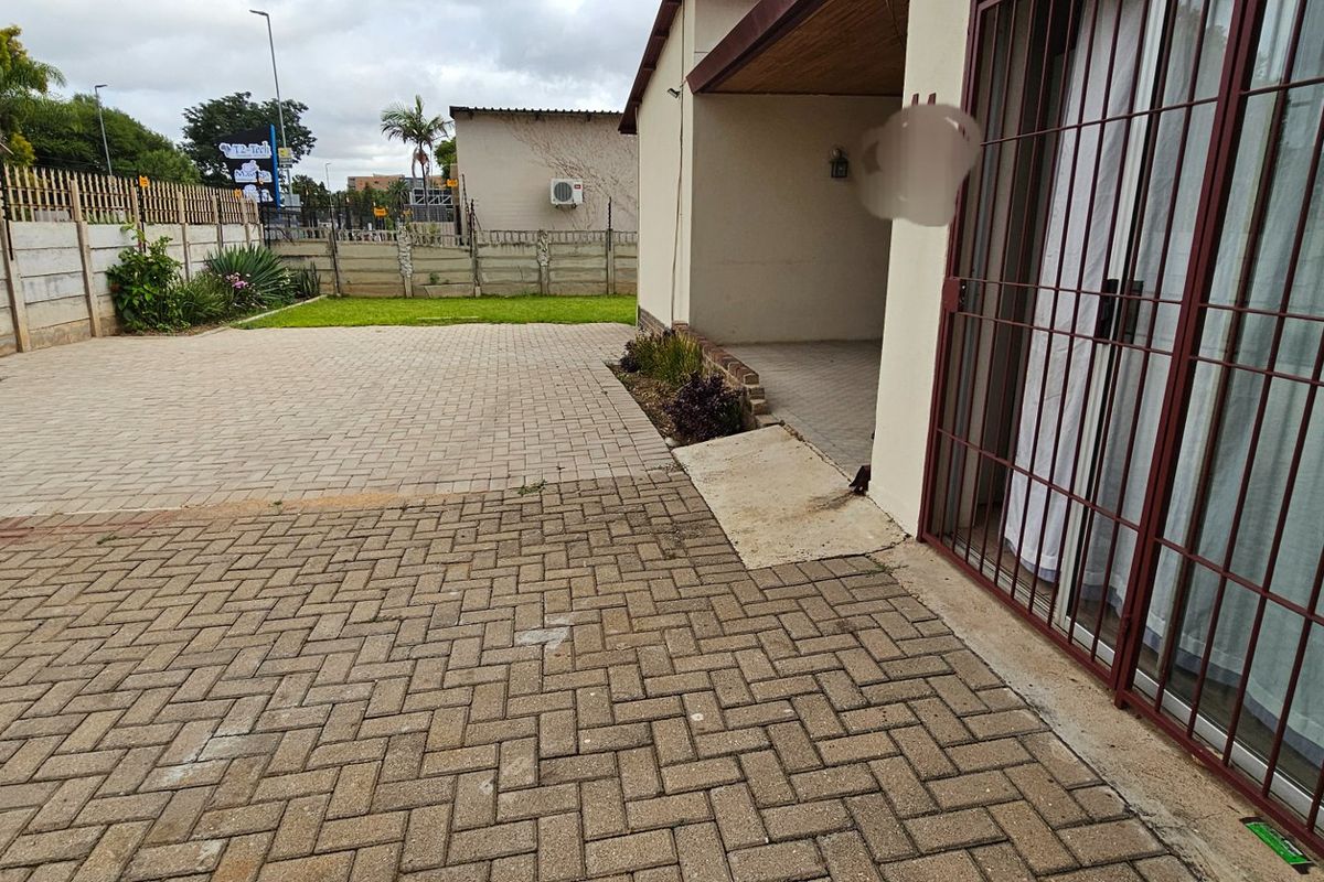 A paved rear courtyard area featuring a covered patio, concrete ramp access, and perimeter walling.