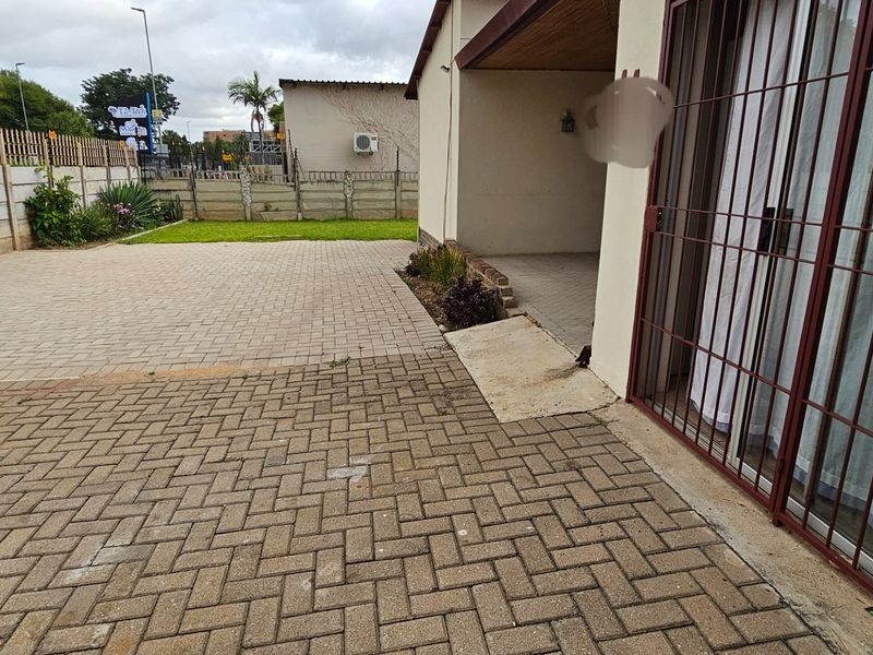 A paved rear courtyard area featuring a covered patio, concrete ramp access, and perimeter walling.