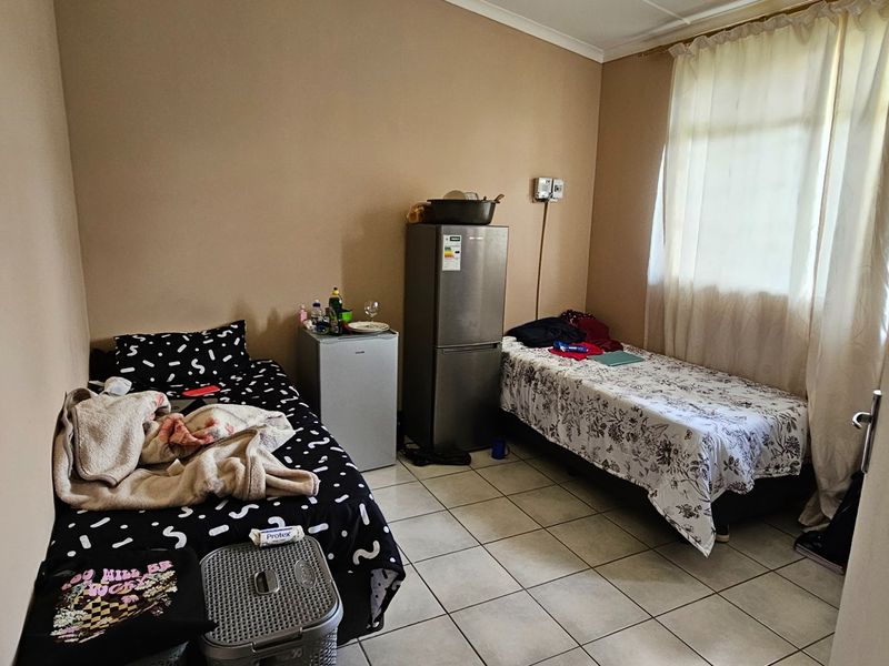 A functional bedroom featuring tiled flooring and a window with curtains, providing a simple and practical living space.