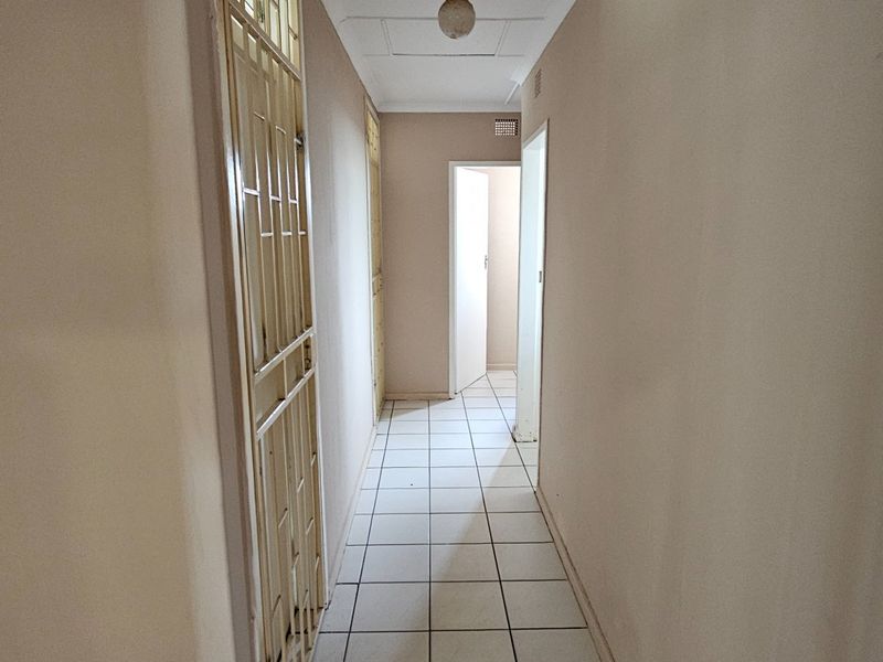 A narrow interior hallway featuring white tiled flooring, neutral wall finishes, and a metal security gate leading to an adjacent room.