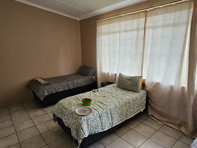 A functional bedroom featuring tiled flooring, built-in wardrobe storage, and large windows with curtains allowing for natural light.