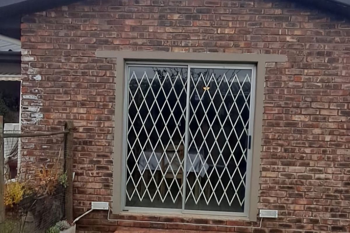 Rear exterior view of a face brick house featuring a sliding glass door with a security gate and brick steps leading to the garden.