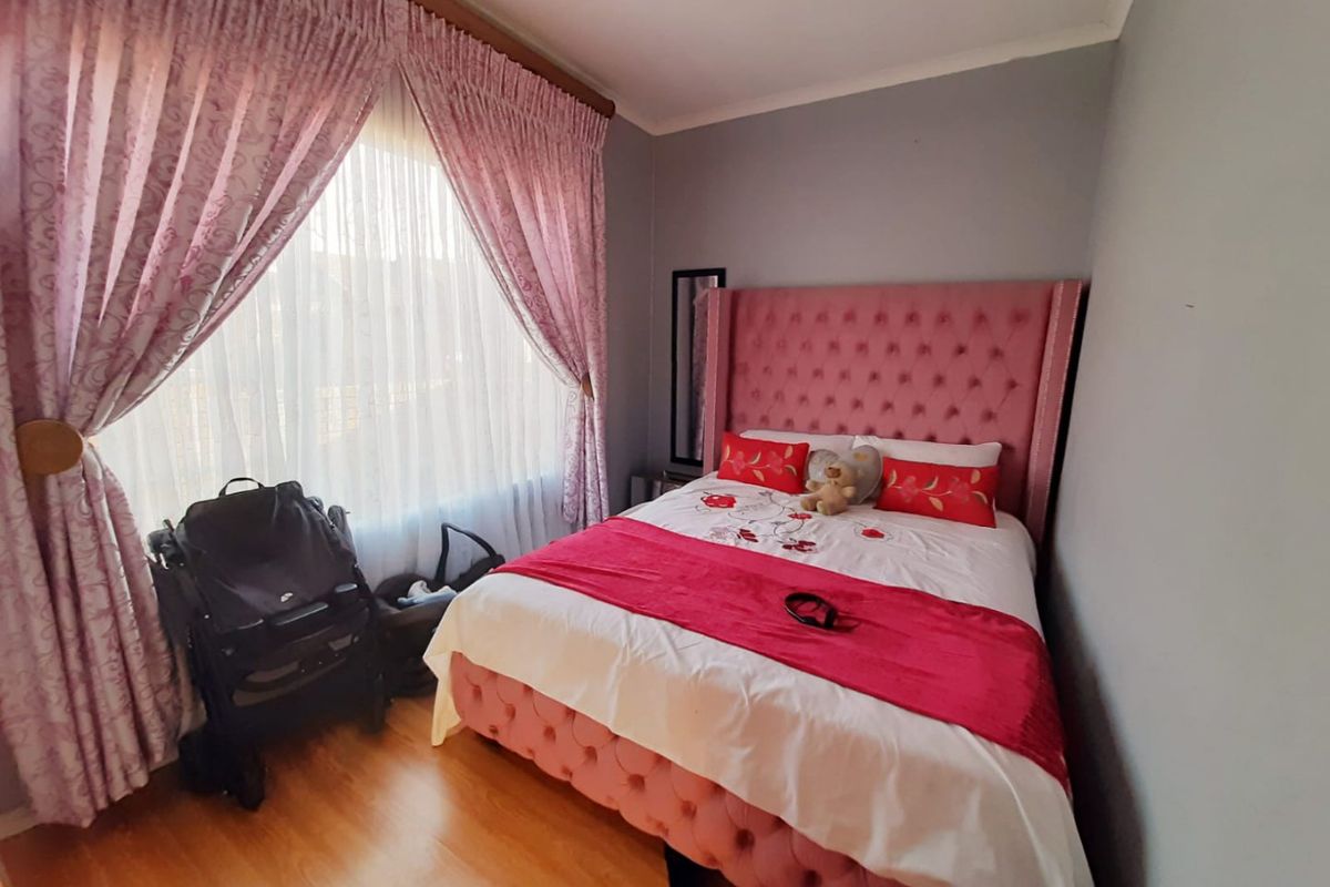 A cozy bedroom featuring laminate flooring and large windows with curtain treatments, providing a comfortable and functional sleeping space.