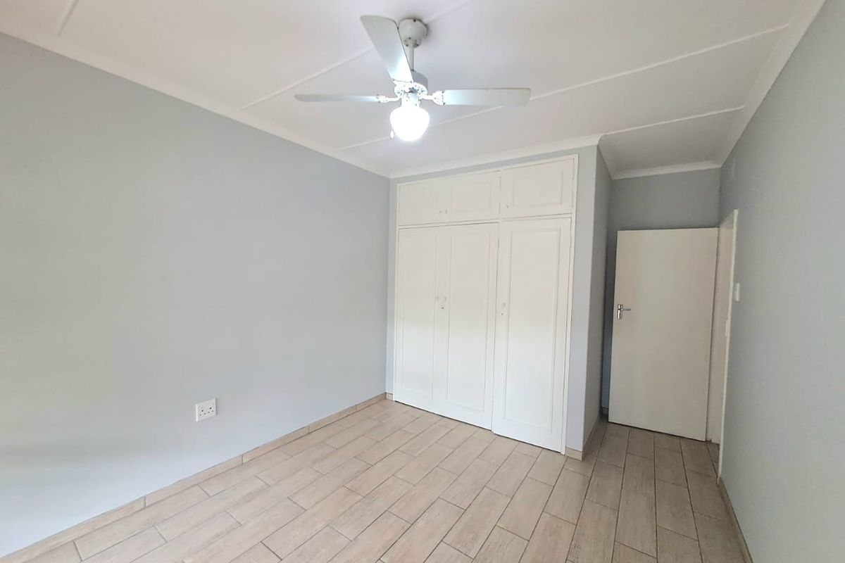 A clean, empty bedroom featuring neutral wall tones, tiled flooring, built-in cupboards, and a ceiling fan.