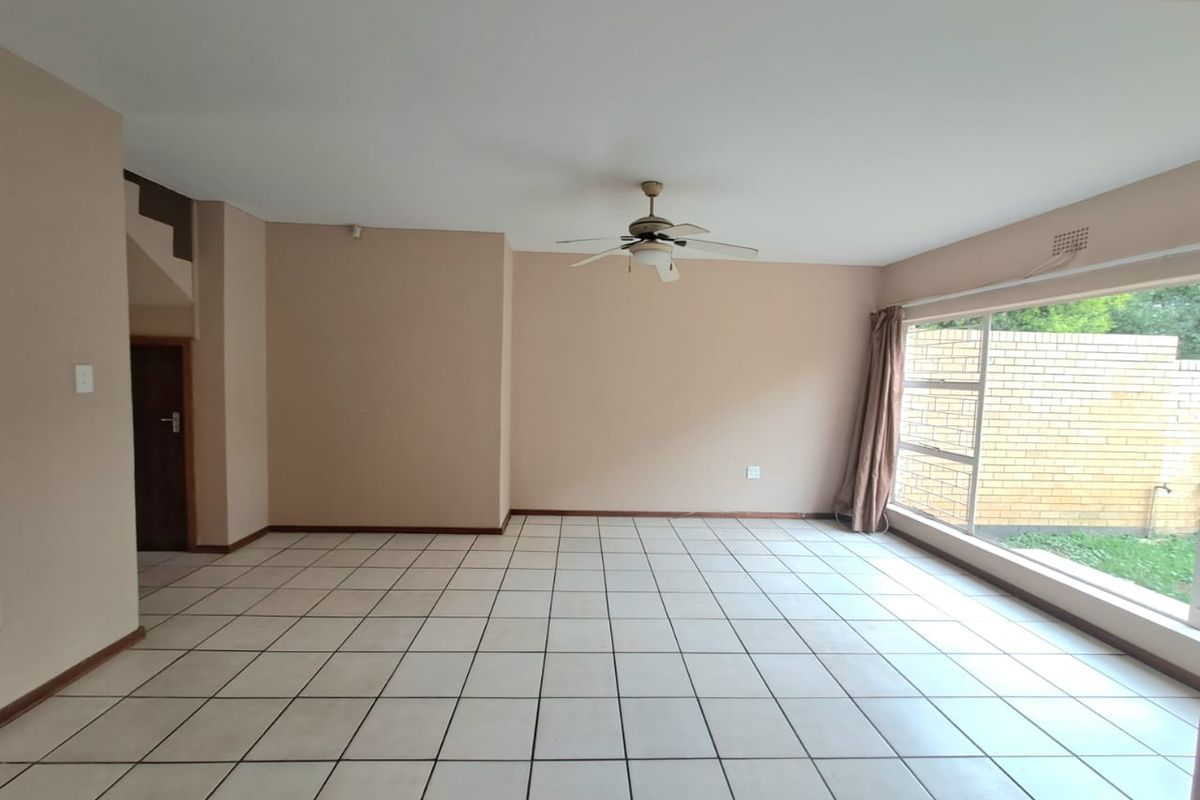 Spacious, empty living area featuring neutral tiled flooring, a ceiling fan, and large windows providing natural light and a view of the rear garden.
