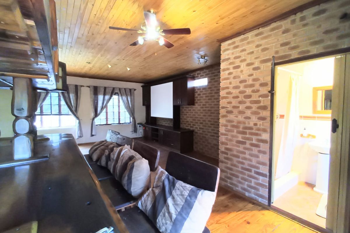 A rustic living area featuring a timber-clad ceiling, exposed brick wall, built-in cabinetry, and an adjoining bathroom.