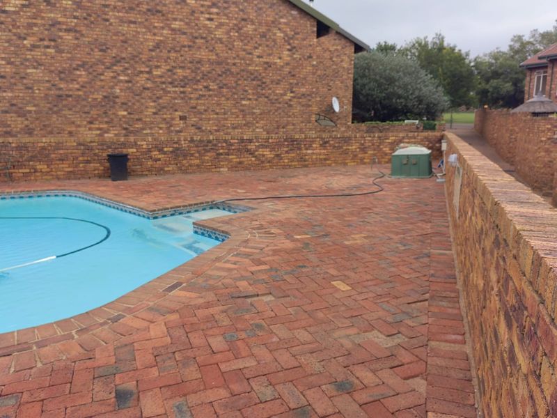 Outdoor pool area featuring a swimming pool surrounded by brick paving and enclosed by a brick boundary wall.