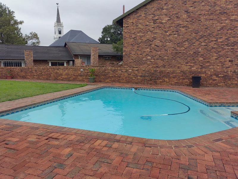A private outdoor swimming pool area featuring brick paving, a well-maintained lawn, and a solid brick boundary wall.