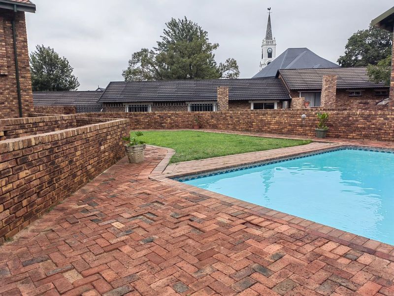 A private outdoor pool area featuring brick paving, a well-maintained lawn, and a secure brick boundary wall.