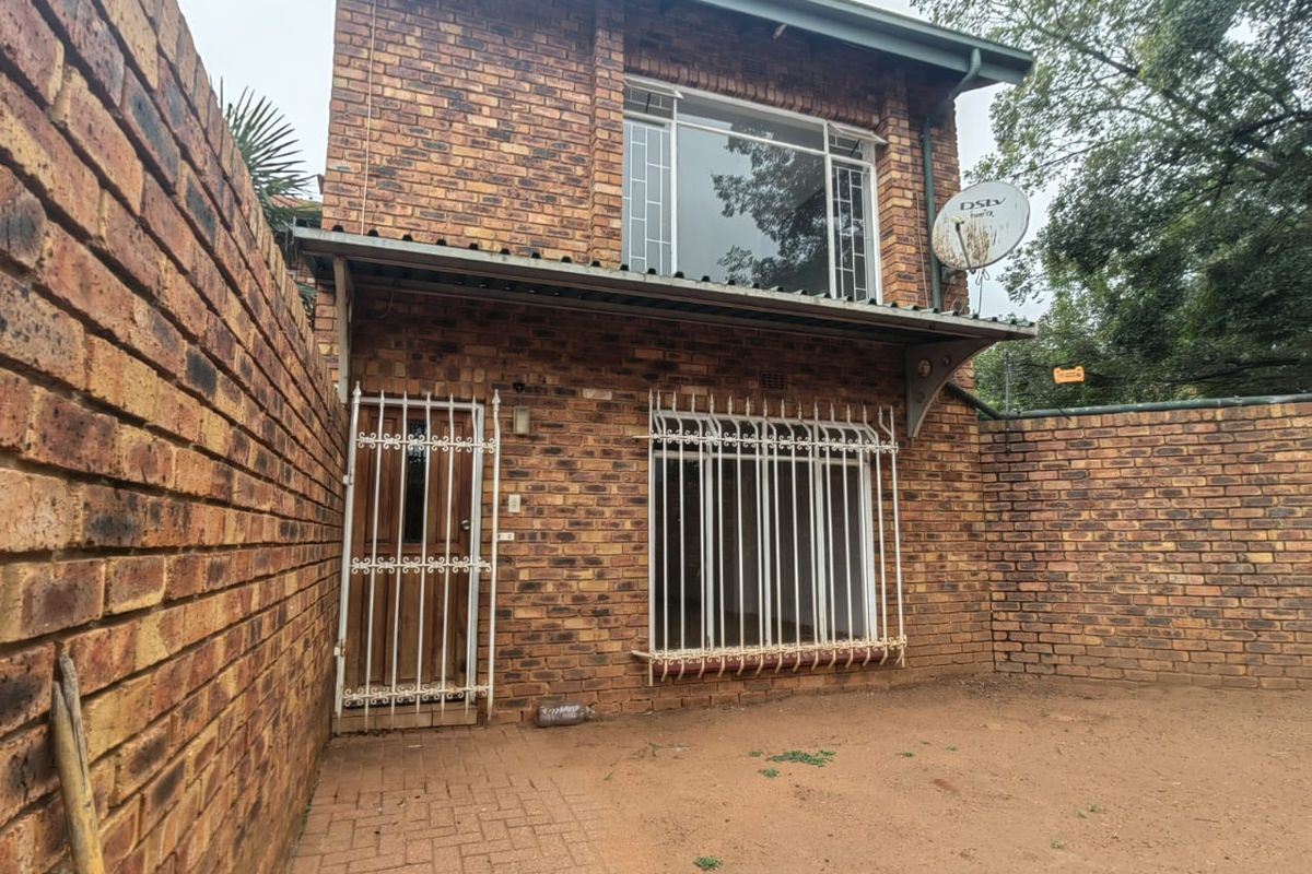 Rear view of a two-story face-brick townhouse featuring security bars on windows and doors, a paved walkway, and an enclosed private yard area.