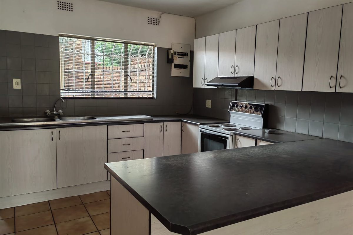 A functional kitchen featuring laminate cabinetry, dark countertops, tiled splashbacks, and a built-in extractor fan, offering a clean and practical workspace.