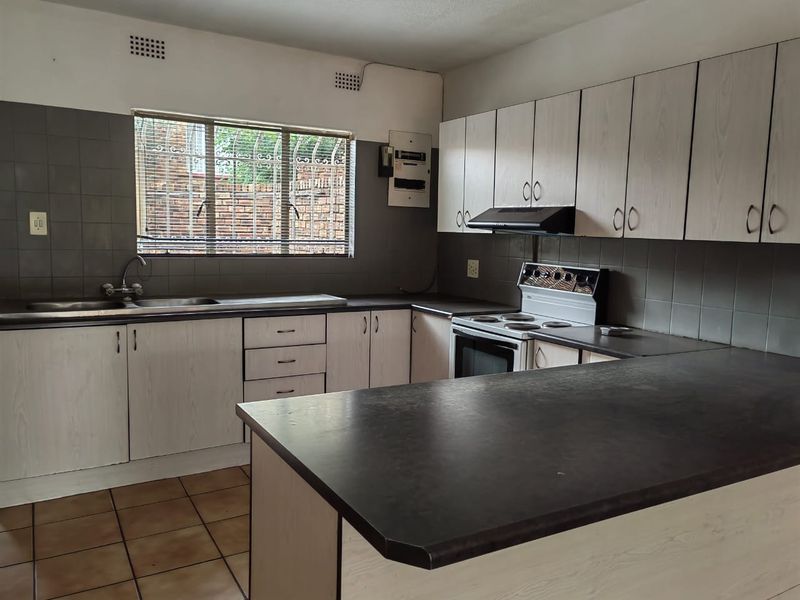 A functional kitchen featuring laminate cabinetry, dark countertops, tiled splashbacks, and a built-in extractor fan, offering a clean and practical workspace.