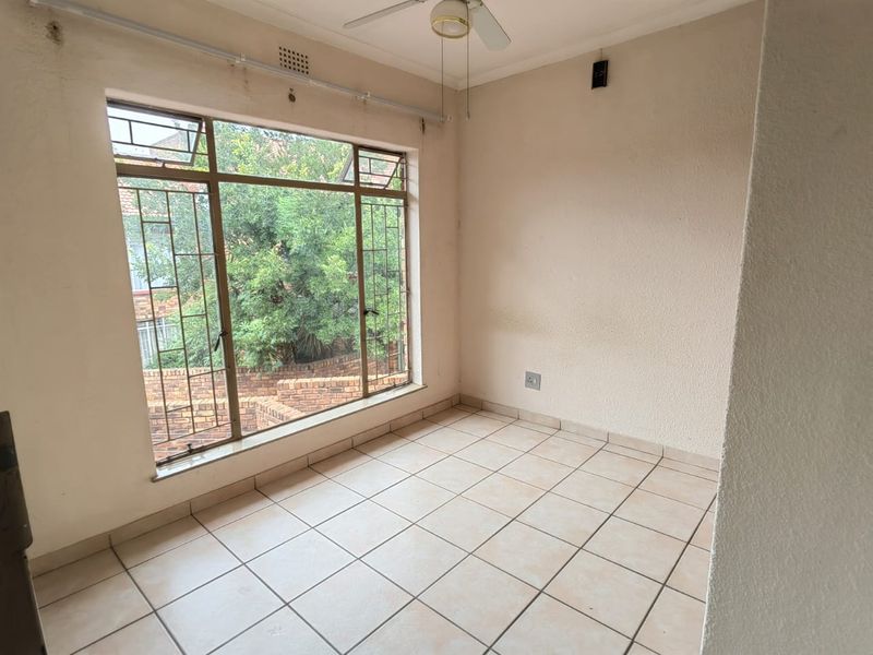 An empty bedroom featuring tiled flooring, a ceiling fan, and large windows with security bars, offering a blank canvas for renovation.