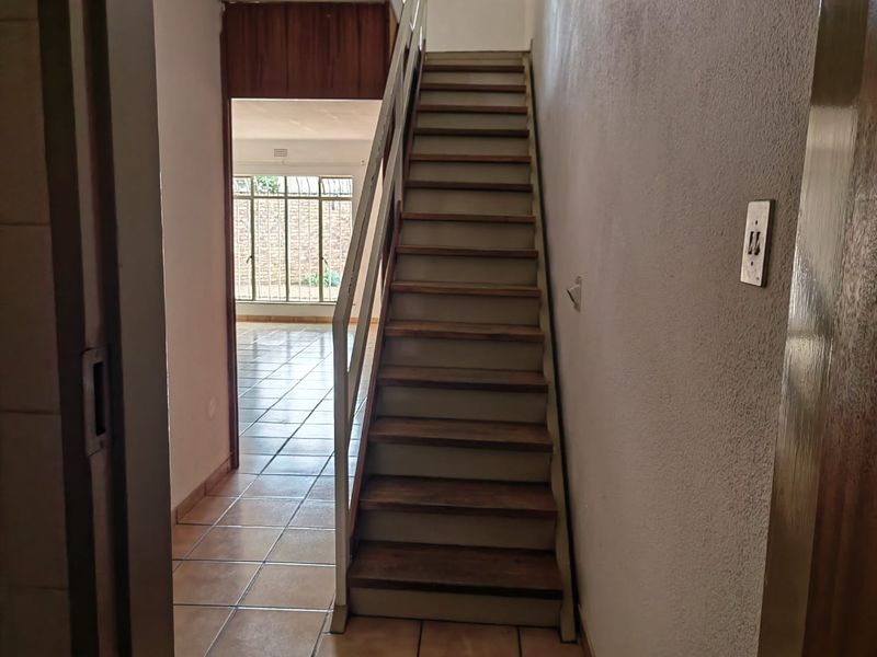 A functional hallway featuring a central staircase with tiled flooring, leading towards an open living area with security bars on the windows.