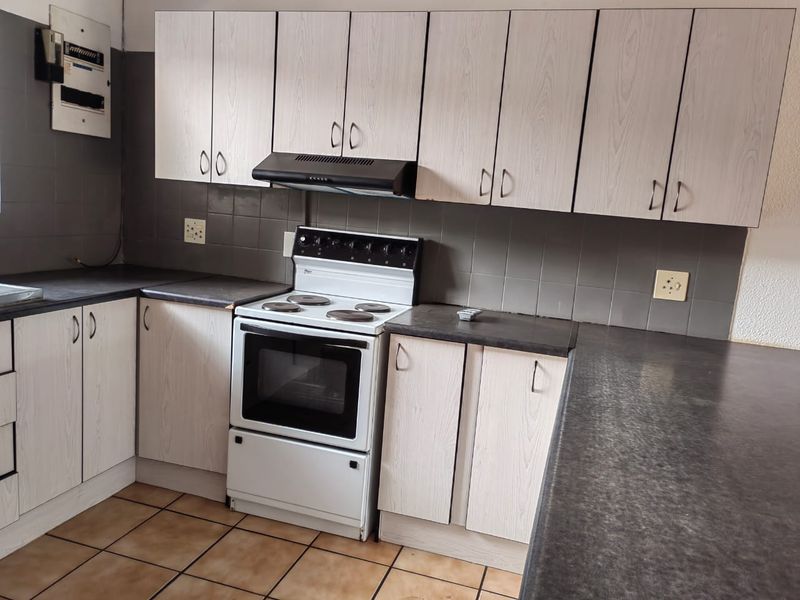 A functional kitchen featuring light-toned laminate cabinetry, dark countertops, a freestanding electric stove with extractor fan, and tiled flooring.