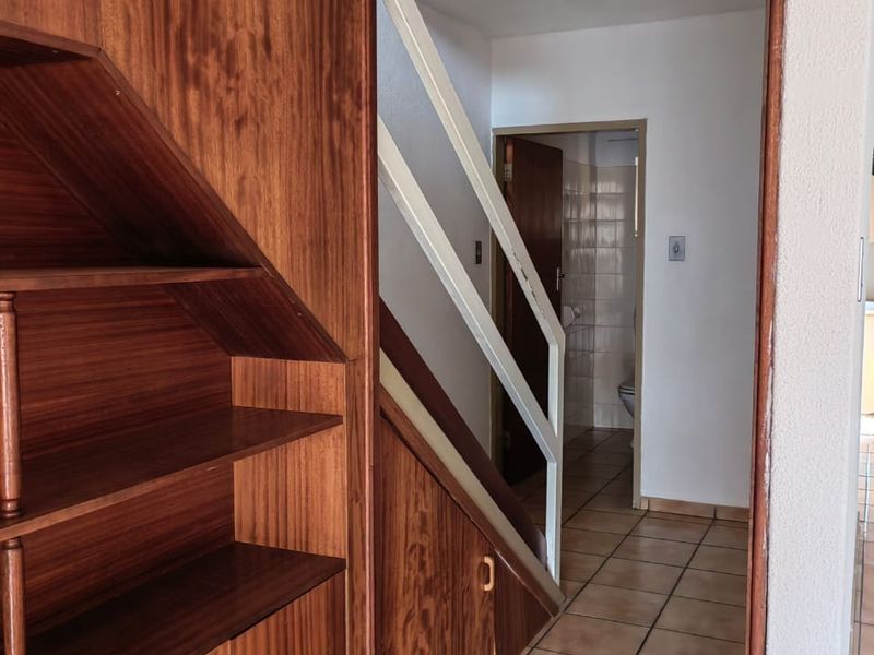 A hallway featuring built-in wooden cabinetry, a staircase, and tiled flooring, leading towards a bathroom area.