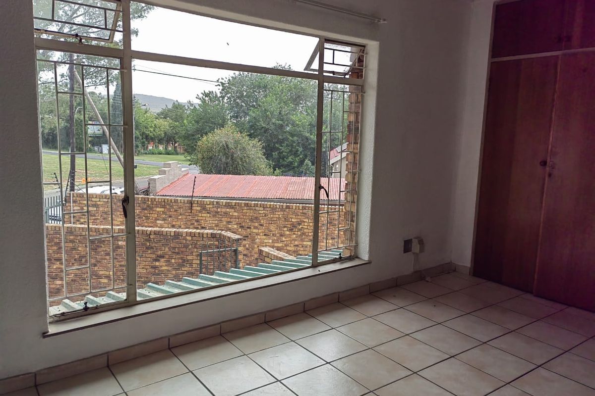 An empty bedroom featuring tiled flooring, a large metal-framed window with security bars, and a built-in wooden wardrobe.